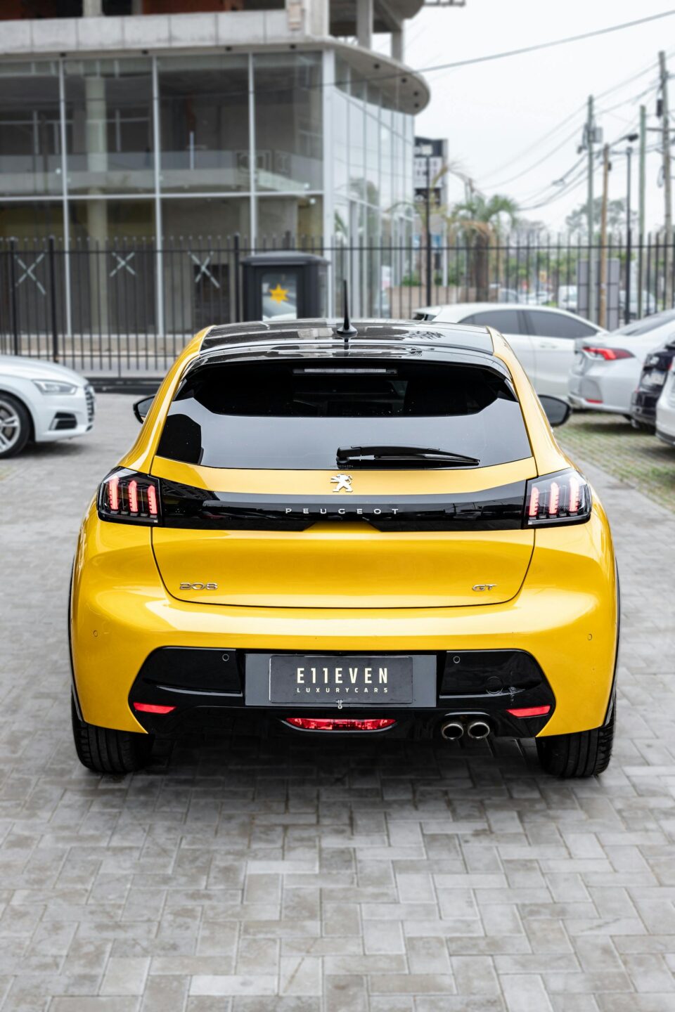 Rear view of a yellow Peugeot 208 GT parked in an urban environment.