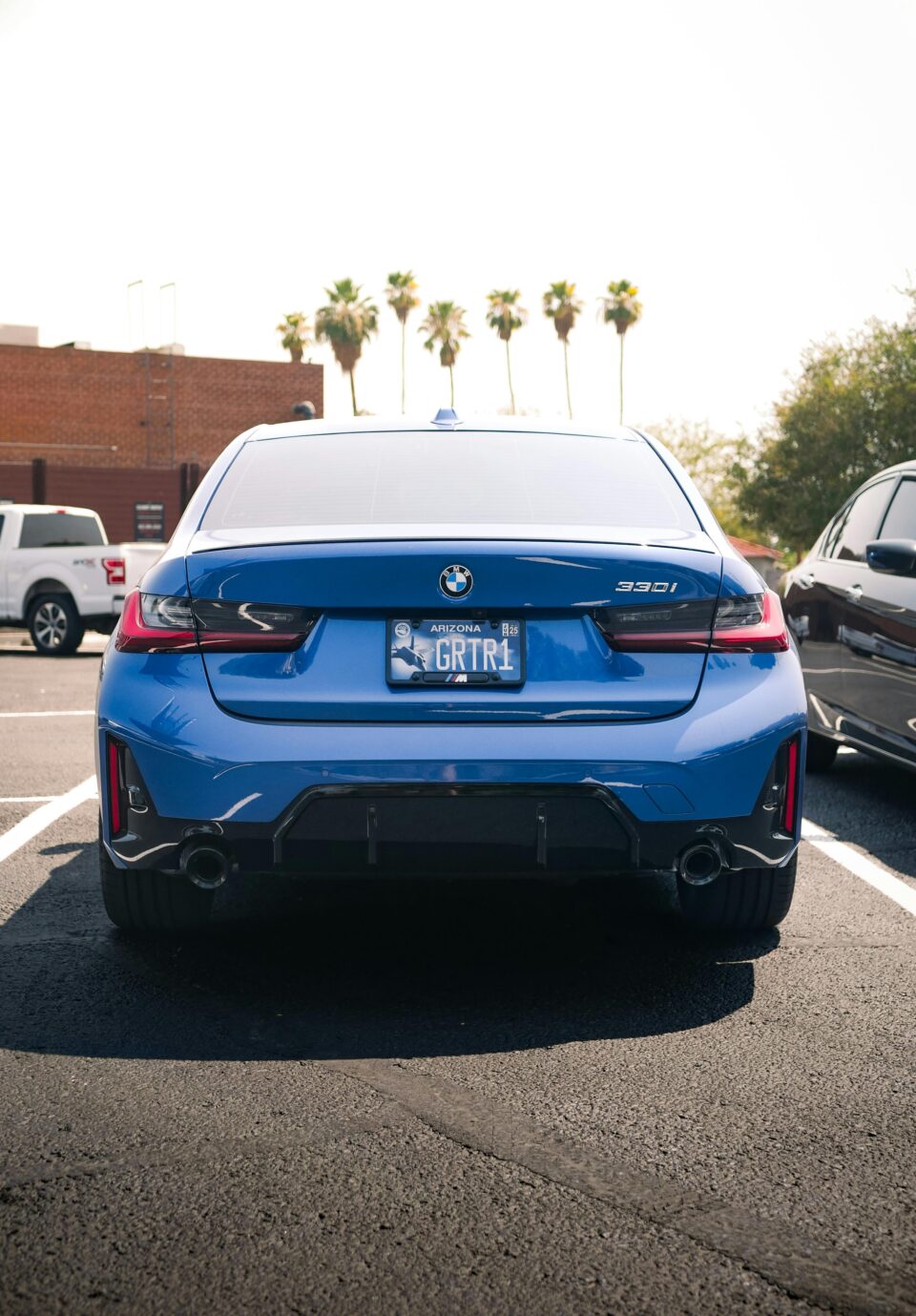 Stunning blue BMW 330i parked in a sunlit lot with palm trees in the background.