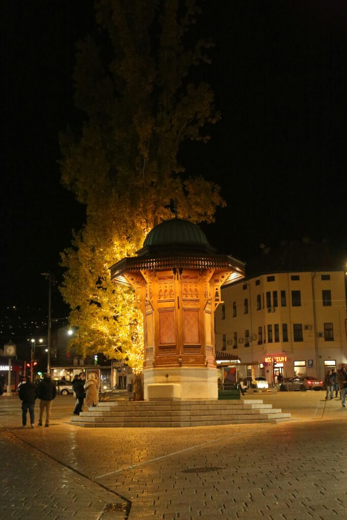pexels-photo-30133312-30133312 Night view of the iconic Sebilj fountain in Sarajevo's Baščaršija square, glowing under lights.