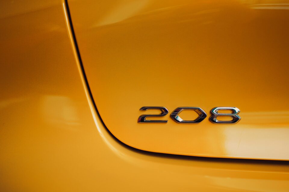 Glossy silver emblem on a vibrant yellow car showcasing the number 208.